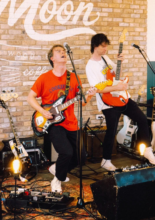 two young men play guitar and singing in a small room