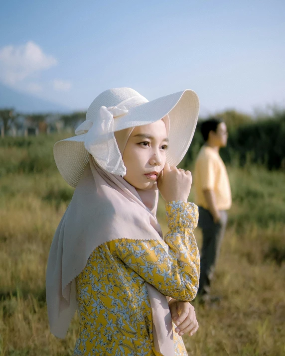 a girl in a yellow dress and white hat standing by a man