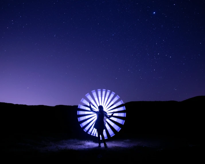 a man standing next to a light up windmill in a dark field