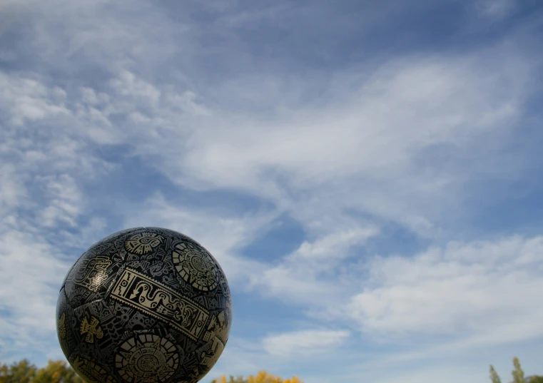 a tall black ball sits under a cloudy blue sky
