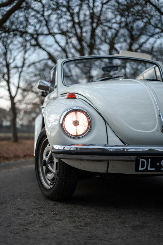 the front end of a white volkswagen beetle car parked on a road