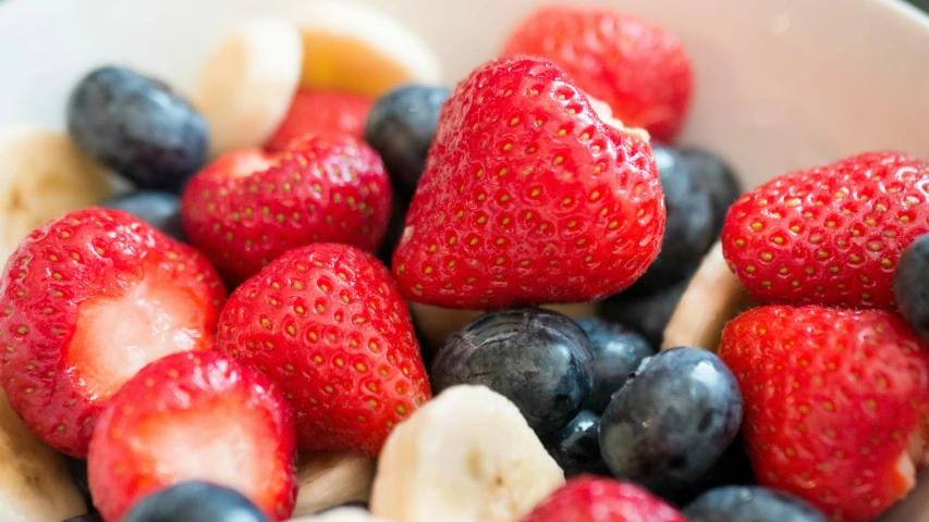 strawberries, bananas and blueberries are in a bowl