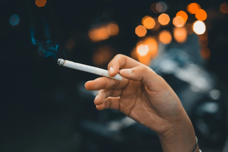 a hand is lit with a cigarette in front of a group of cars