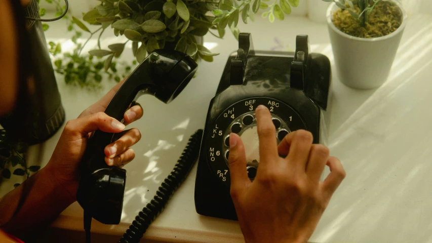 someone holding their hand and pointing to an old style phone on a desk