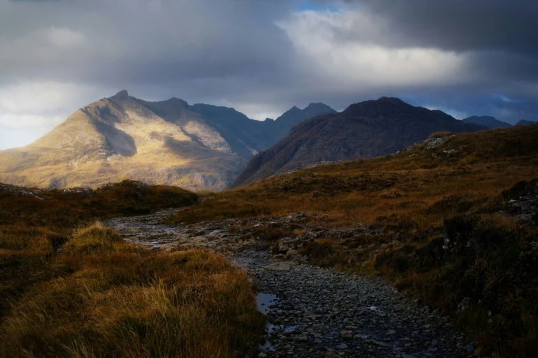 a mountain valley is pictured with a small stream in the foreground