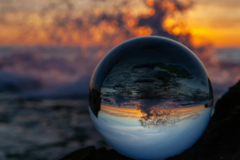 a glass ball reflecting a colorful sunset over the ocean