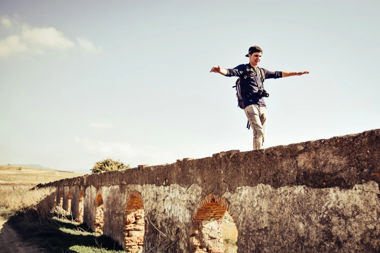 man on a skateboard stands on top of an old brick wall