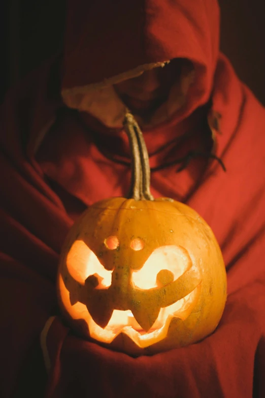 a person in a red hooded jacket holding a carved pumpkin