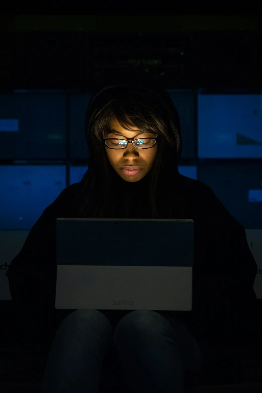a woman sitting in the dark looking at a laptop computer