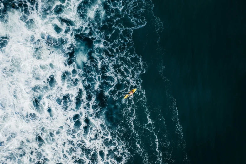 yellow canoe on ocean next to rocks in foamy water