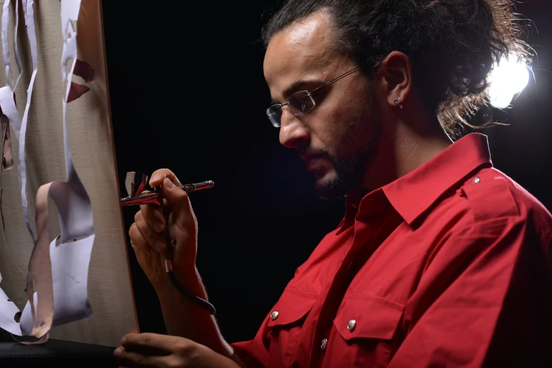 man with dreadlocks doing painting of red shirt