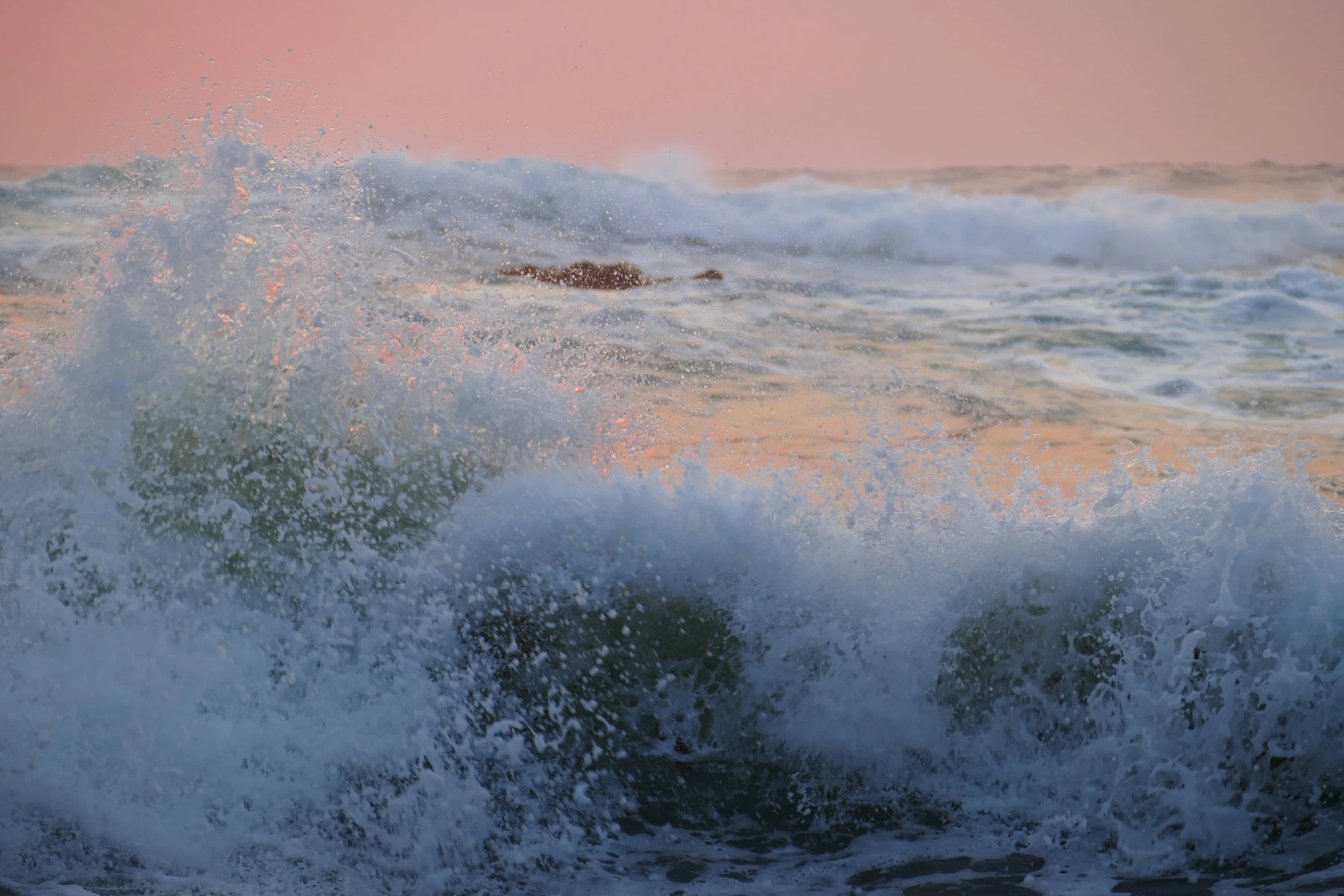 a wave crashes and spreads as the sun sets