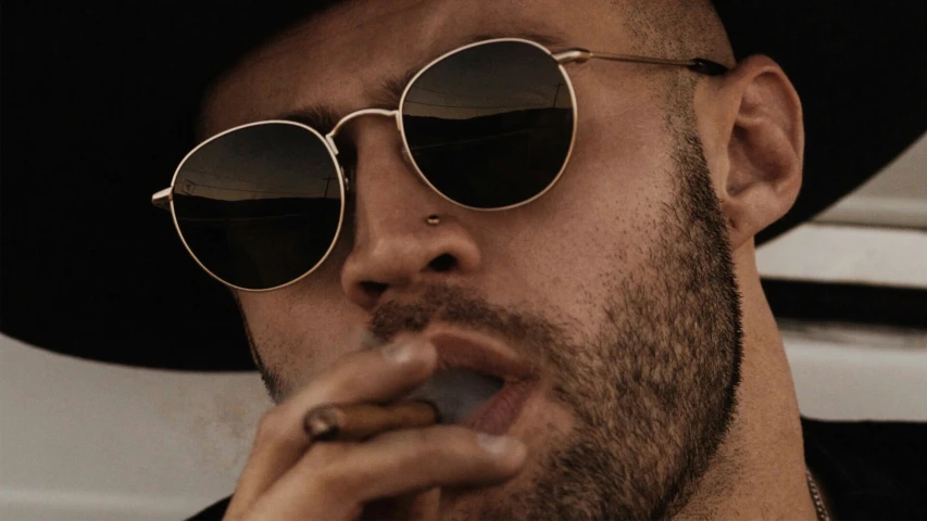 the man wearing the hat and glasses smokes a cigarette