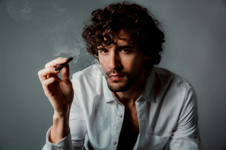 a man in white shirt holding cigarette in front of grey background