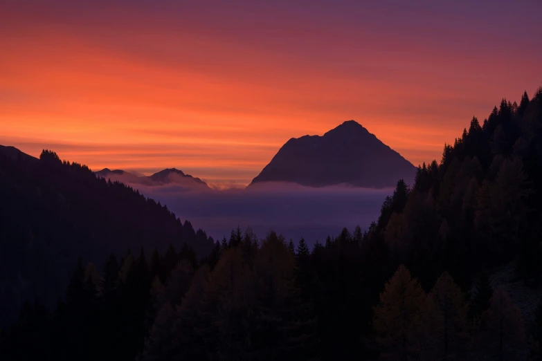 a sunset view of a mountain top with clouds around it