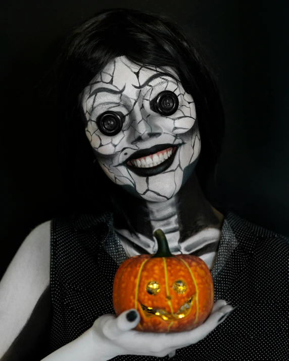 a female wearing an artistic white and black costume holds up a jack o lantern pumpkin