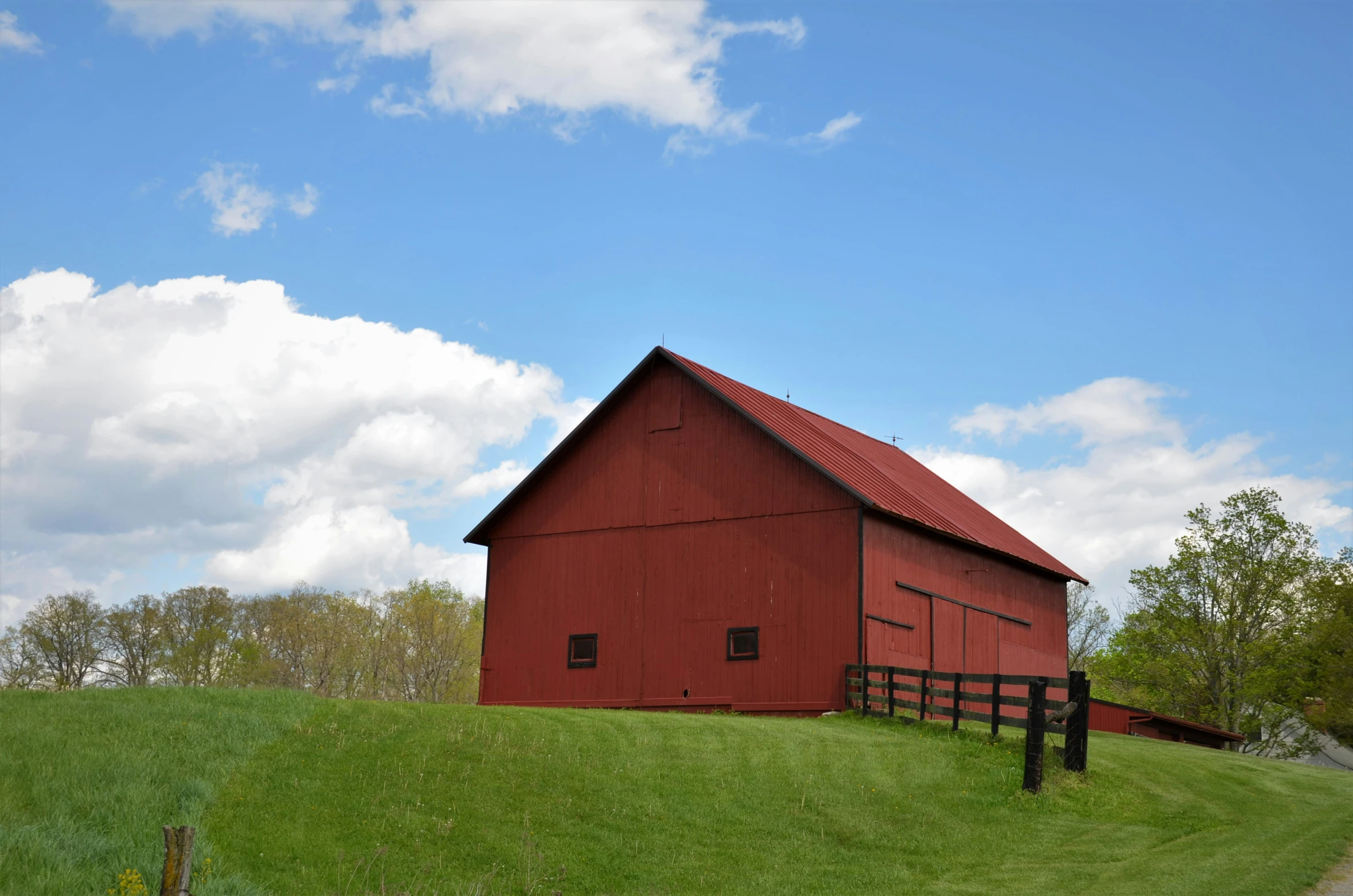 a farm field with a large red barn next to the road