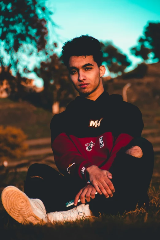 a young man sitting in grass wearing a red shirt