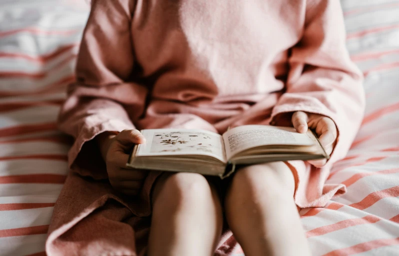 a woman is sitting on her bed while reading a book