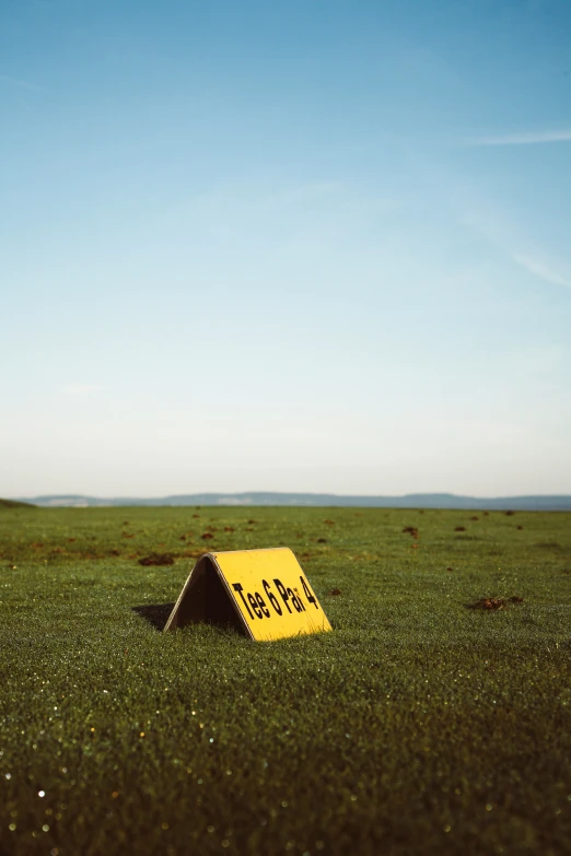 a yellow tent on the grass with a sign on it