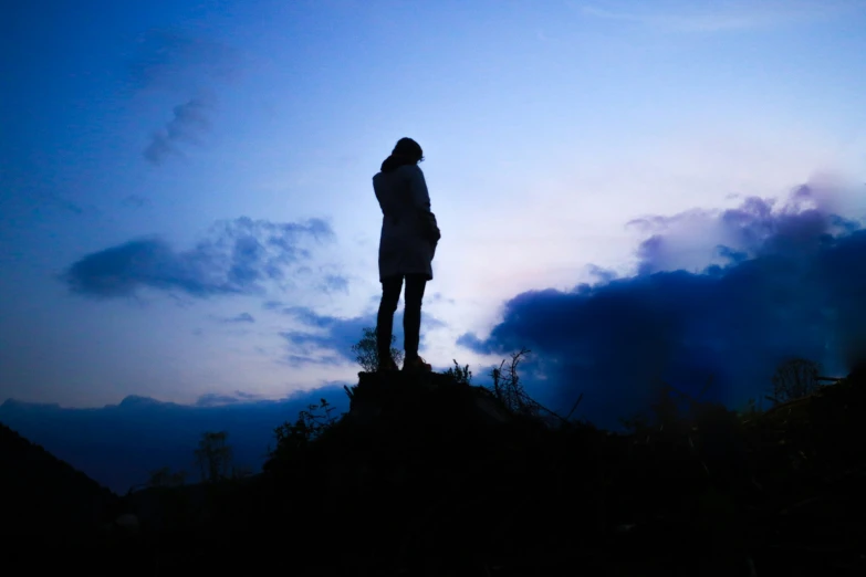 person standing at the top of a hill, overlooking the blue sky and puffy clouds