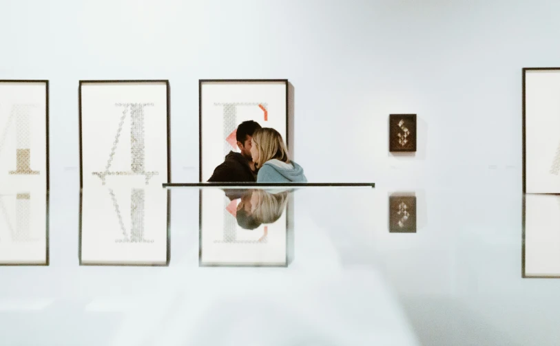 two people leaning up against a wall in an art gallery