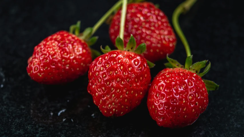 three strawberries sitting on top of a black counter