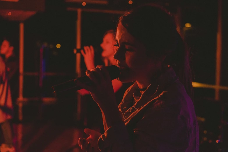 a girl on a microphone and a man in a dark room with a window