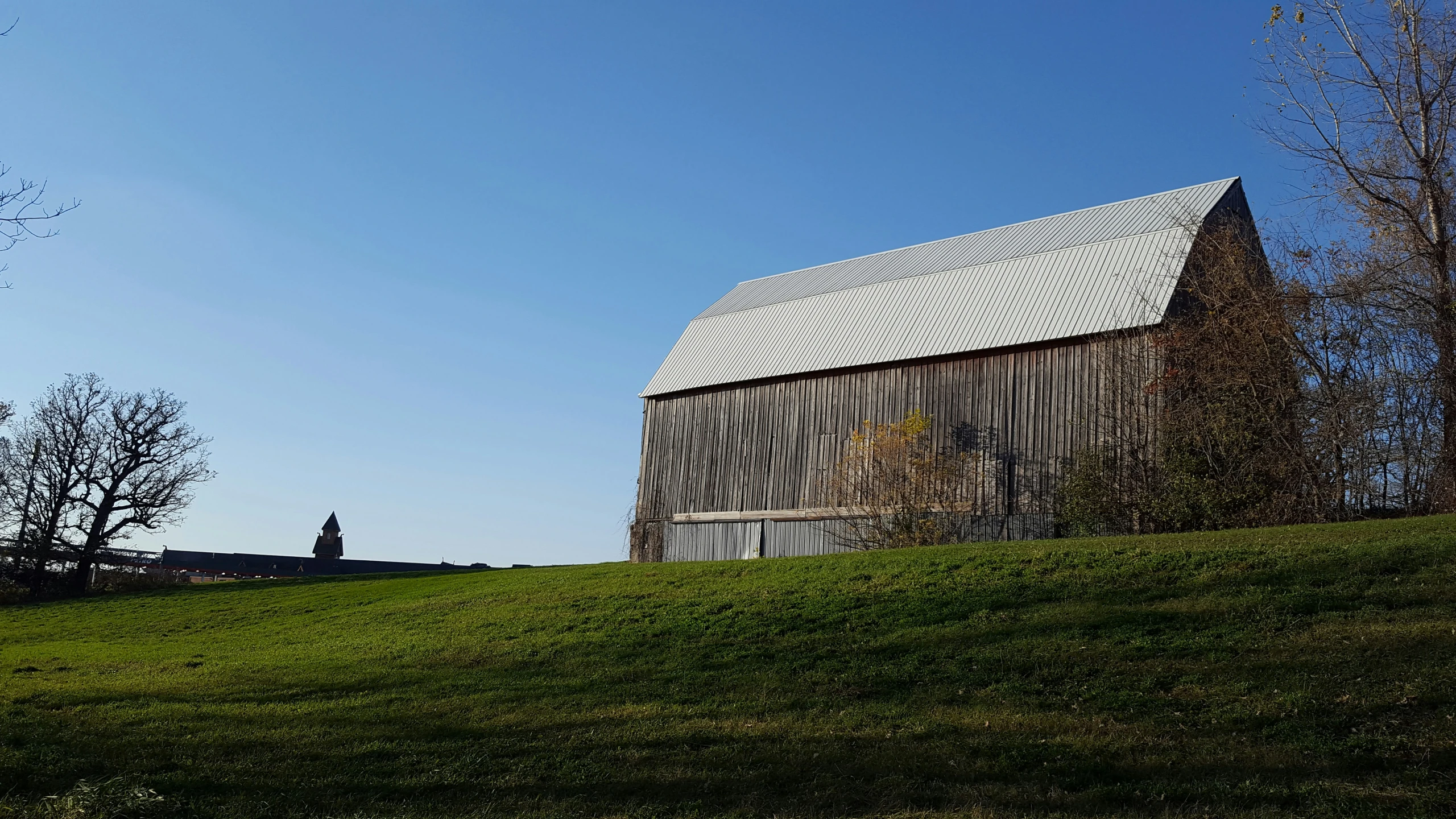 an old barn sits on a hill near the woods