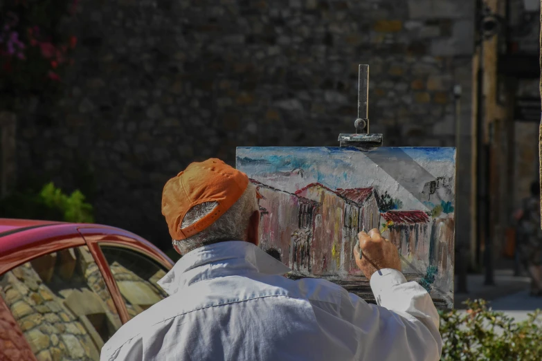 the person is painting outside with an old car nearby