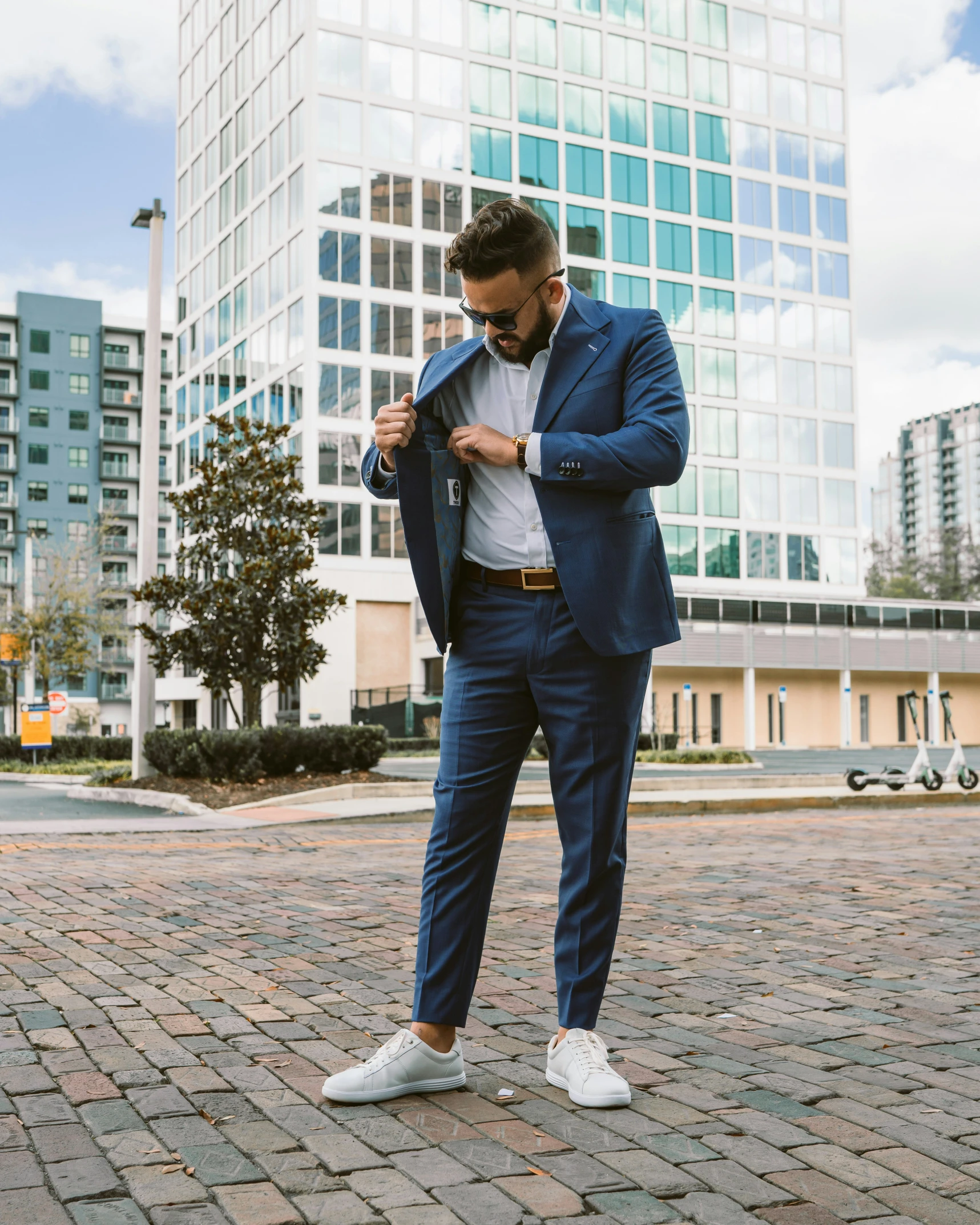 a man wearing a blue suit and white shirt and shoes standing on the sidewalk