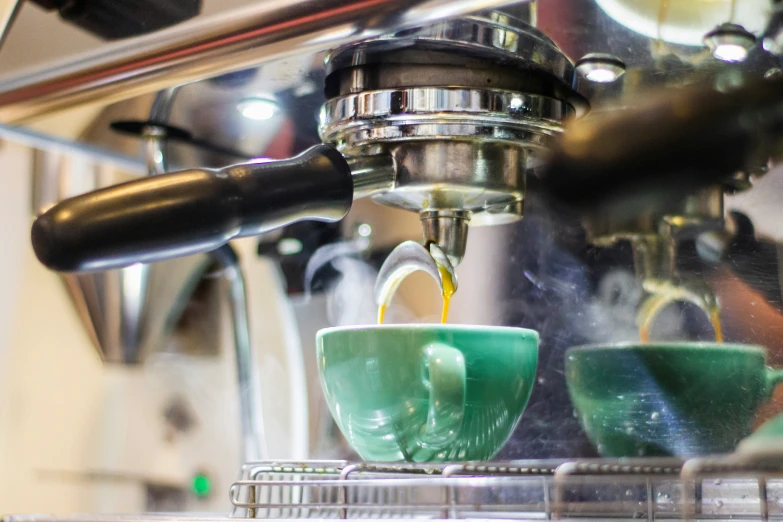 a coffee machine pouring coffee into two green cups