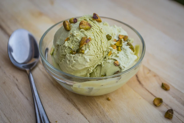 a small bowl with ice cream and pistachios in it next to spoons