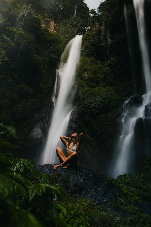 a women is sitting on a rock next to a waterfall