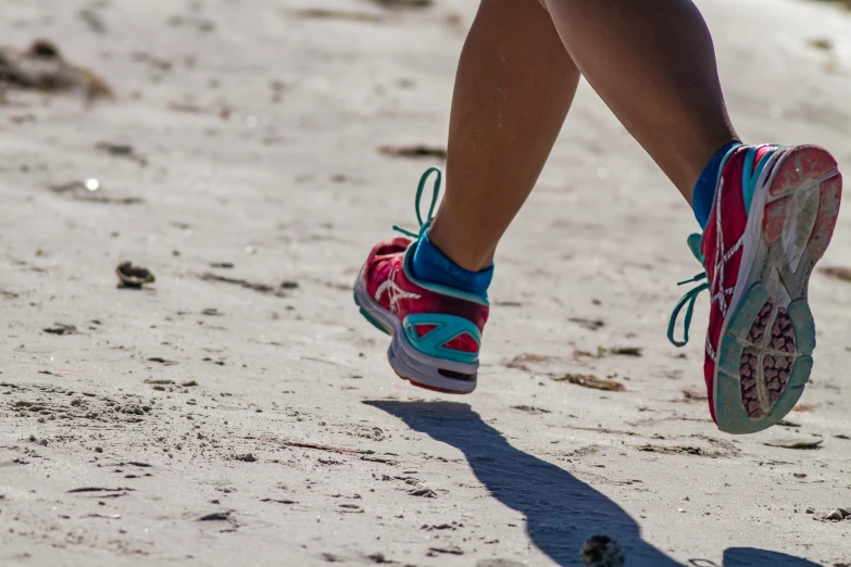 someone in pink and blue running shoes on a sandy beach