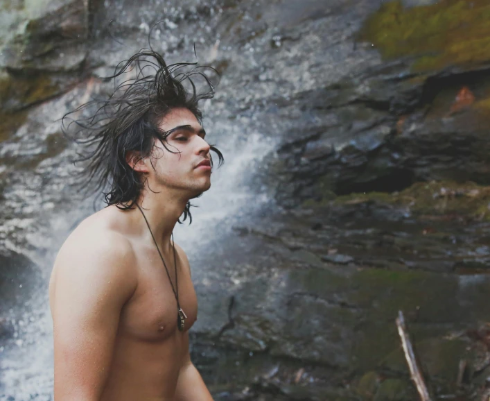 shirtless man with a mohawk looking into a water fall