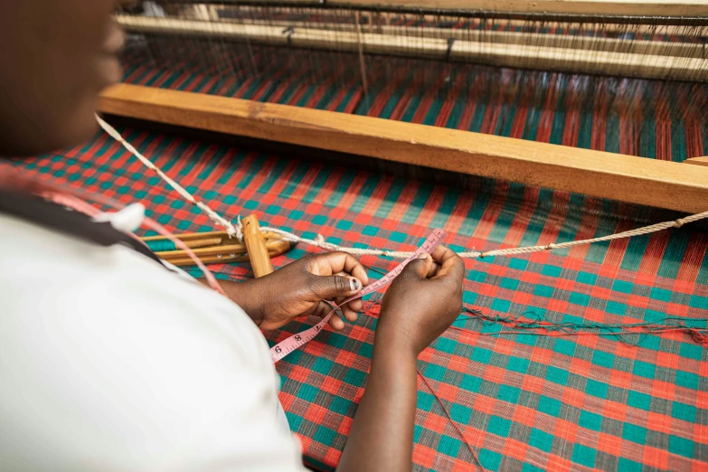 a person using a weaving machine on red and green rug