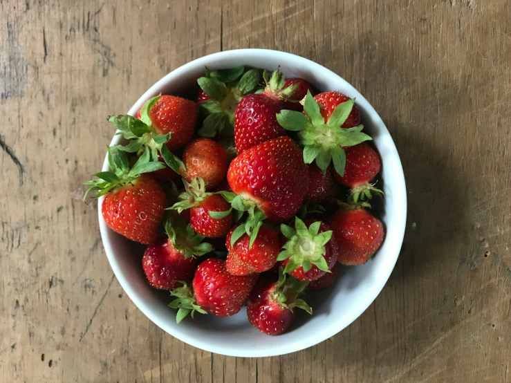 the bowl of strawberries has a green leaf on top of it