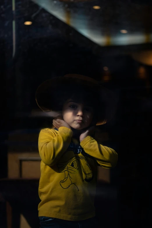 small child in a cowboy hat standing against a window