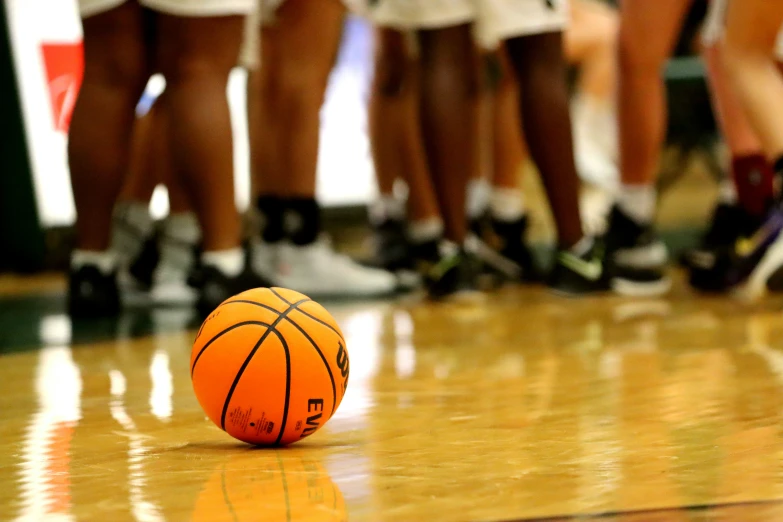 a basketball laying on a hardwood court, near other players