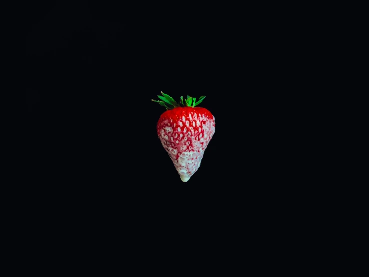 a strawberry shaped object with green stems sitting in the dark