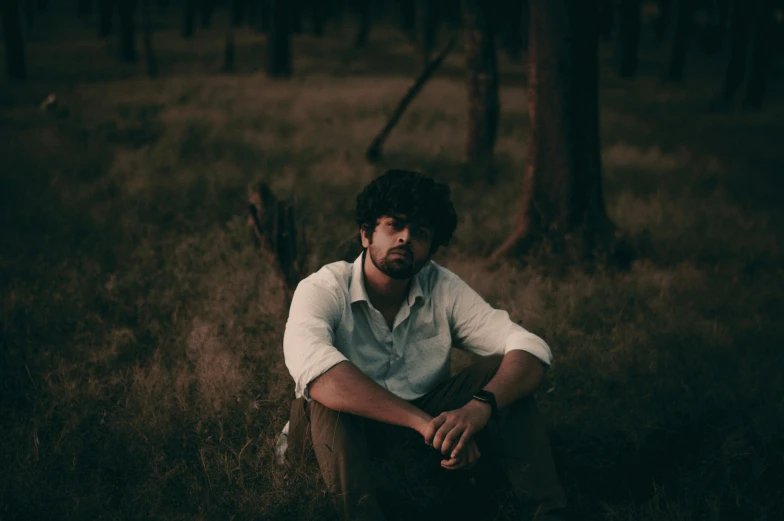 man sitting in field with trees behind him