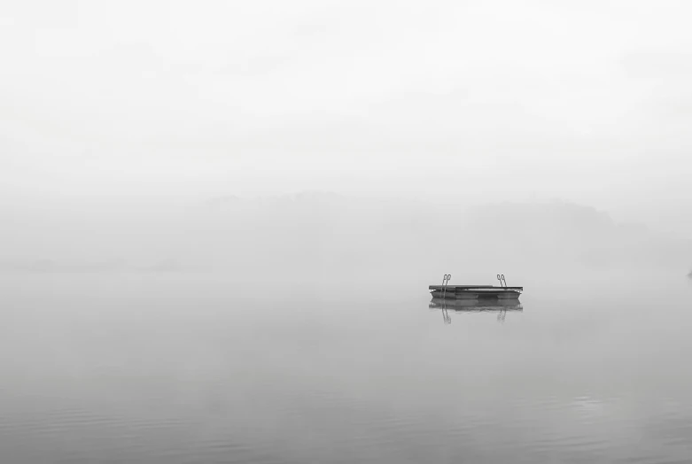 a small boat sitting in the middle of a lake on a foggy day