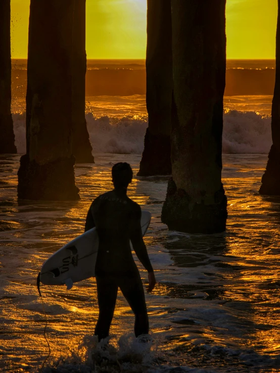 the person walks with a surfboard under several poles