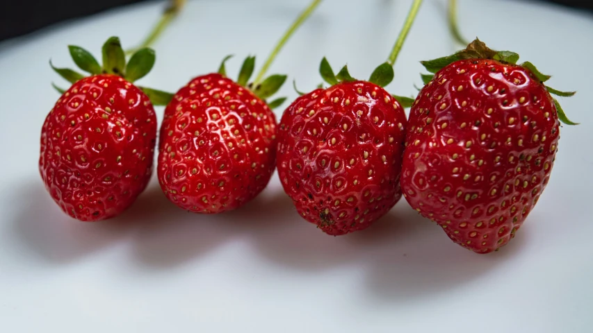 four strawberrys, one big and one small, sit on top of a white surface