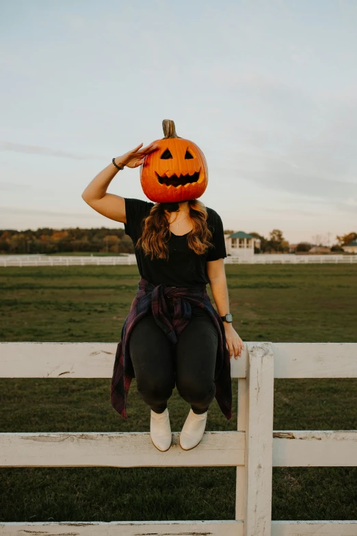 woman with a pumpkin head sitting on a white fence