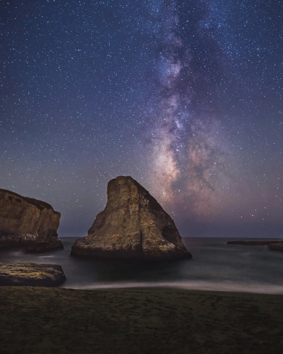 a beach under a stars filled sky next to two large rocks