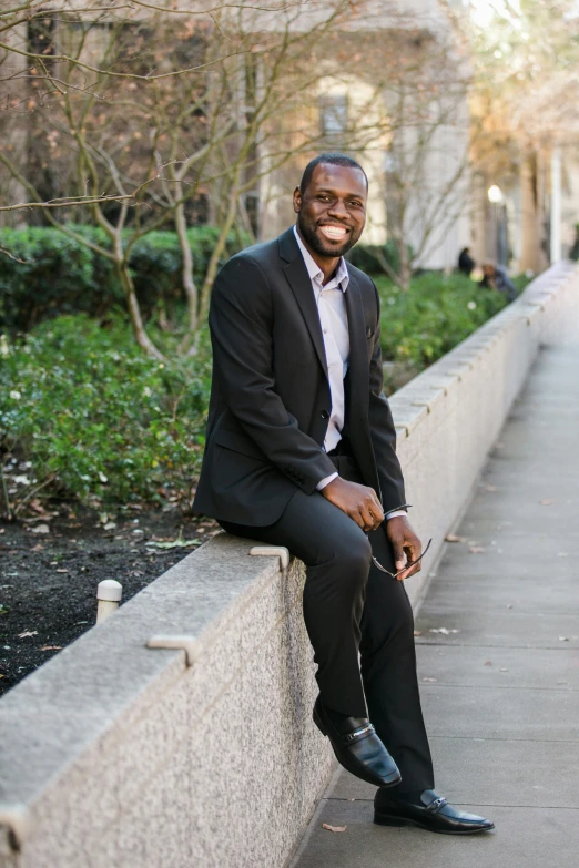 an african american businessman in a business suit, sitting on a wall and smiling