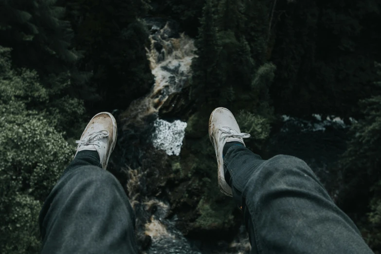 someone with white sneakers standing on rocks looking down at a stream
