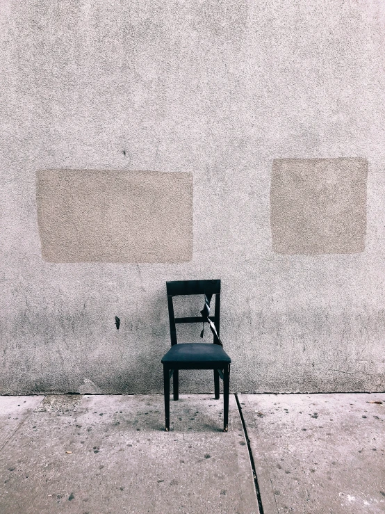 an empty chair on the sidewalk near a wall